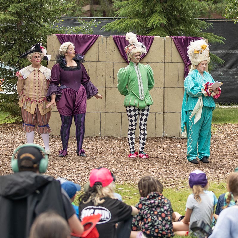 4 actors in play outside with children watching